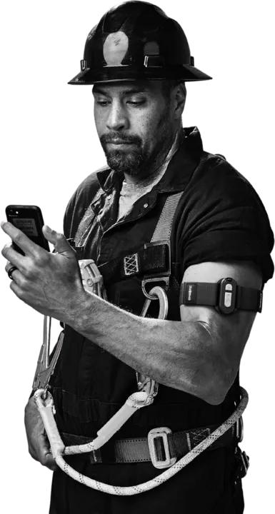 Worker in a hard hat and fall-arrest harness checking the Epicore app on their phone, armband on the upper arm